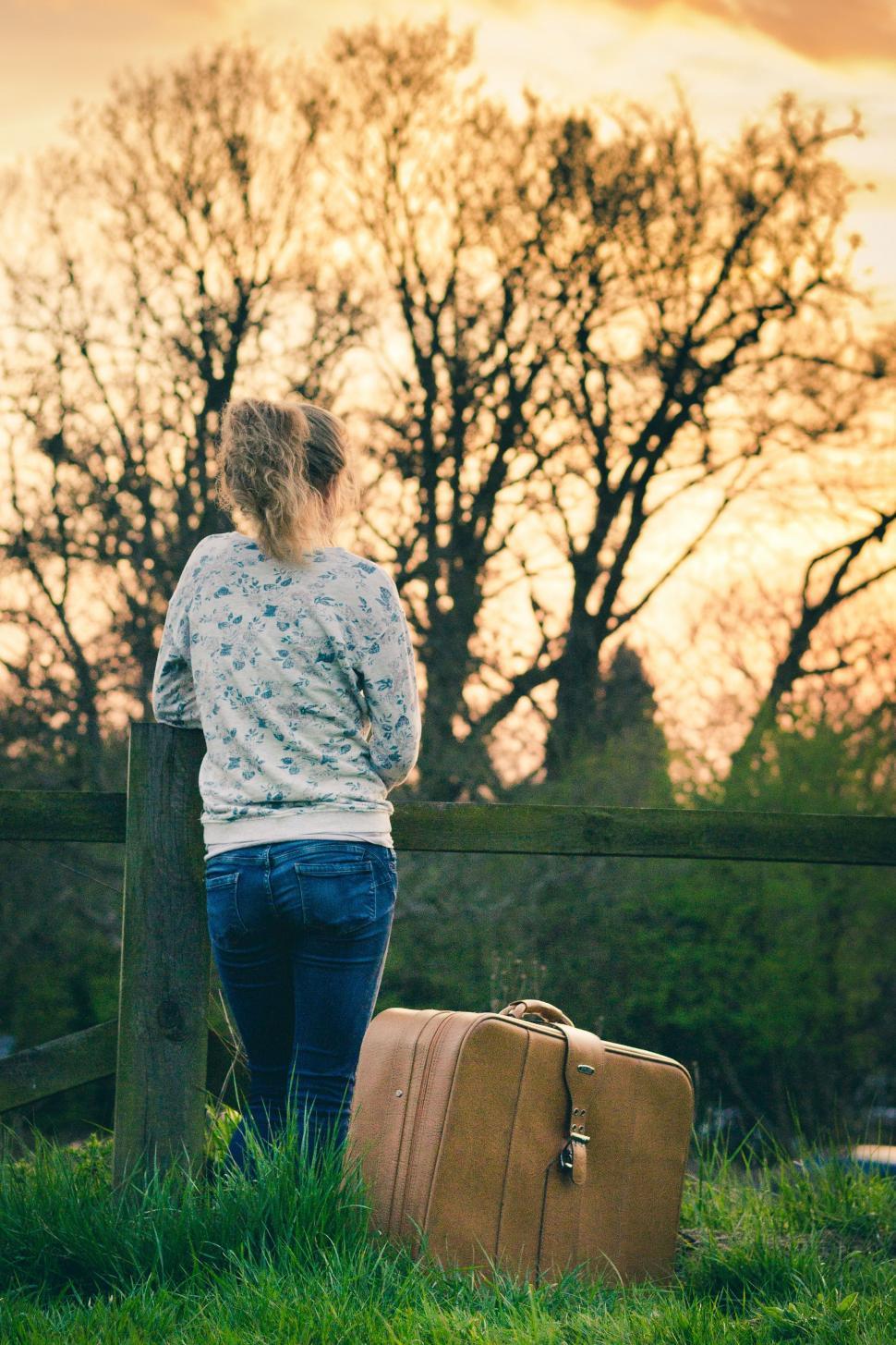 Free Image of Woman Standing Next to Fence With Suitcase 
