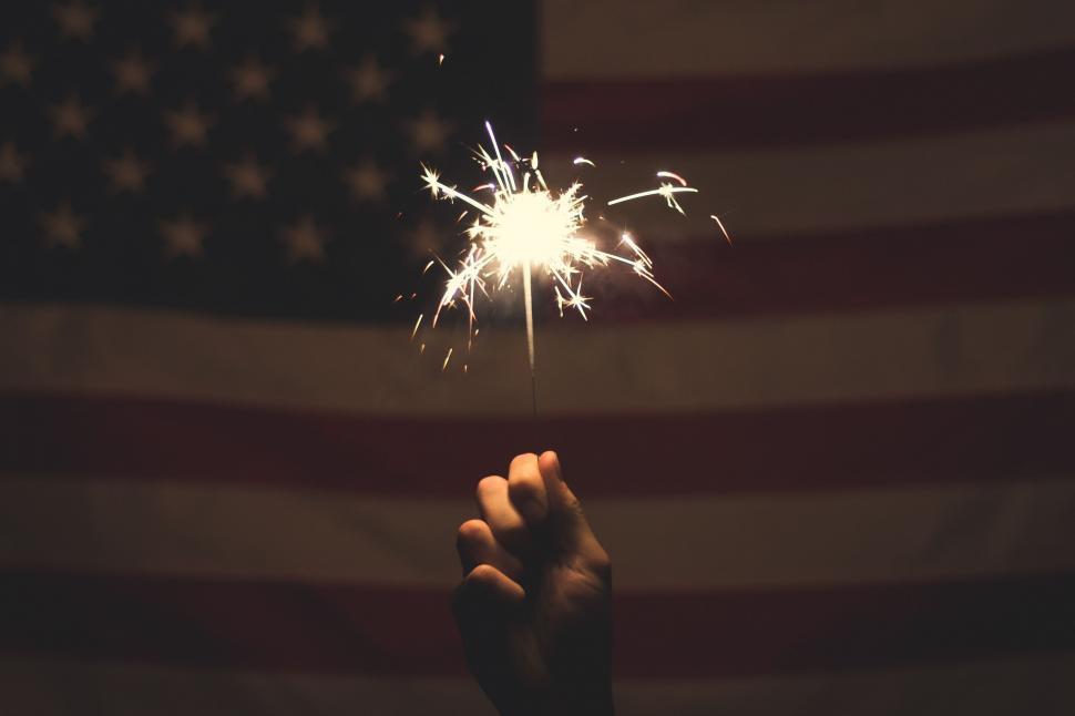 Free Image of Person Holding Sparkler in Front of American Flag 