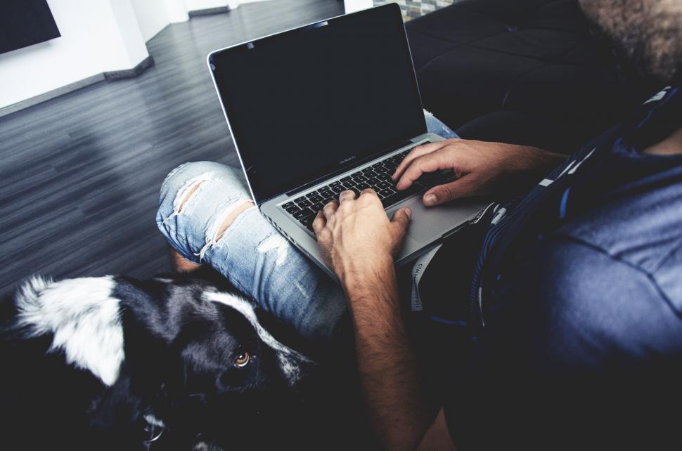 Free Image of Man Sitting on Couch With Laptop Next to Dog 