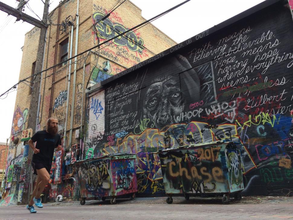 Free Image of Man Running Past Graffiti-Covered Wall 