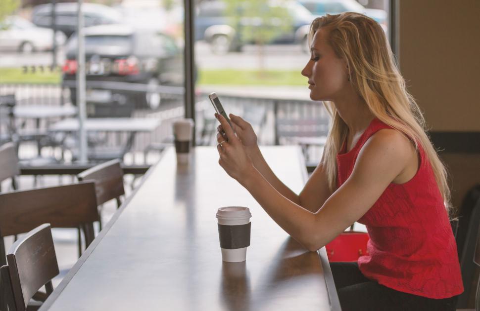 Free Image of Woman Sitting at Table Looking at Cell Phone 