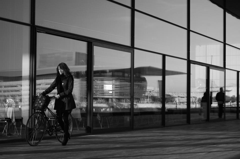 Free Image of Woman Riding Bike Next to Tall Building 