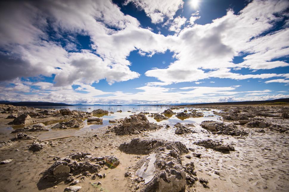 Free Image of Sandy Beach With Rocks and Water Under Cloudy Sky 