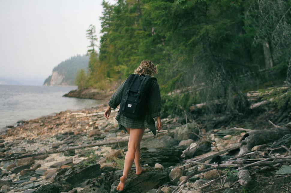 Free Image of Woman Walking Along Rocky Beach by Forest 