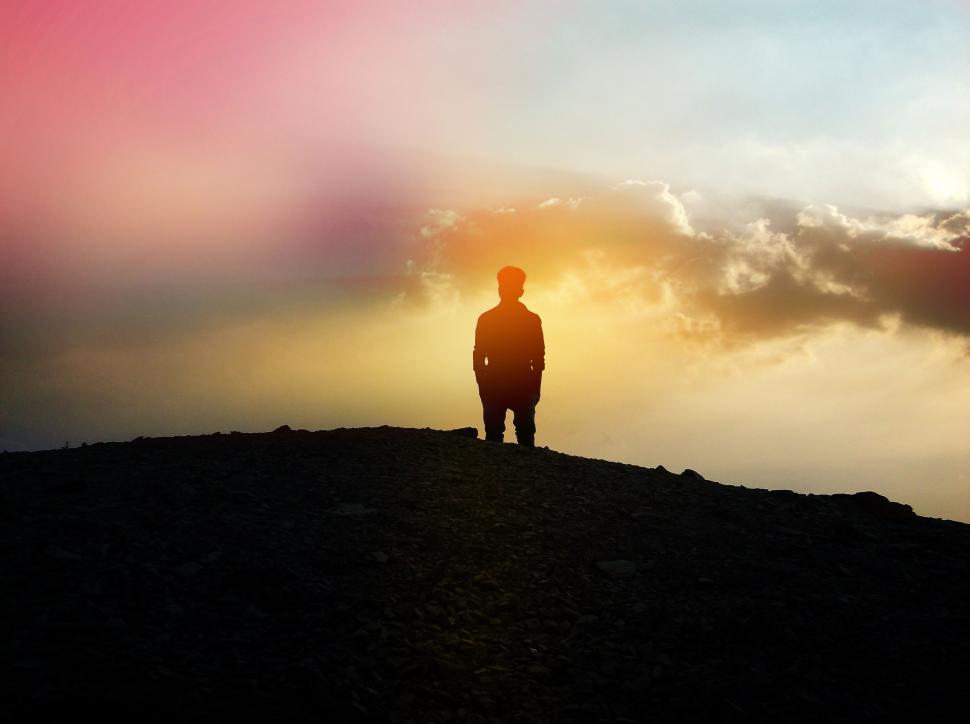Free Image of Man Standing on Top of Hill Under Cloudy Sky 