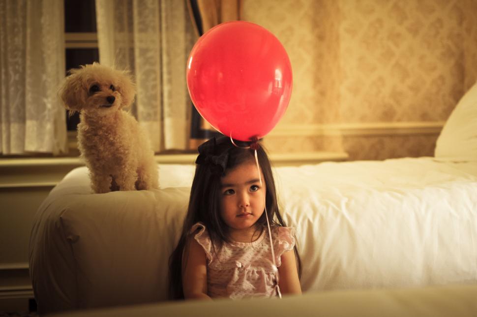 Free Image of Little Girl Sitting on Couch With Red Balloon on Head 