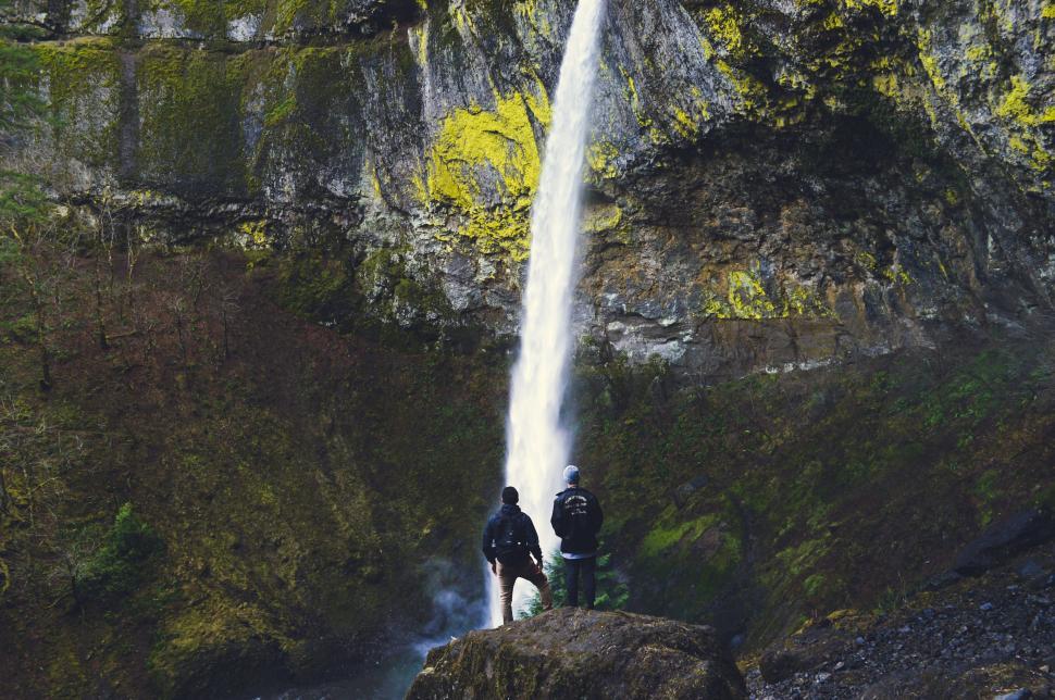 Free Image of Two People Standing at the Base of a Waterfall 