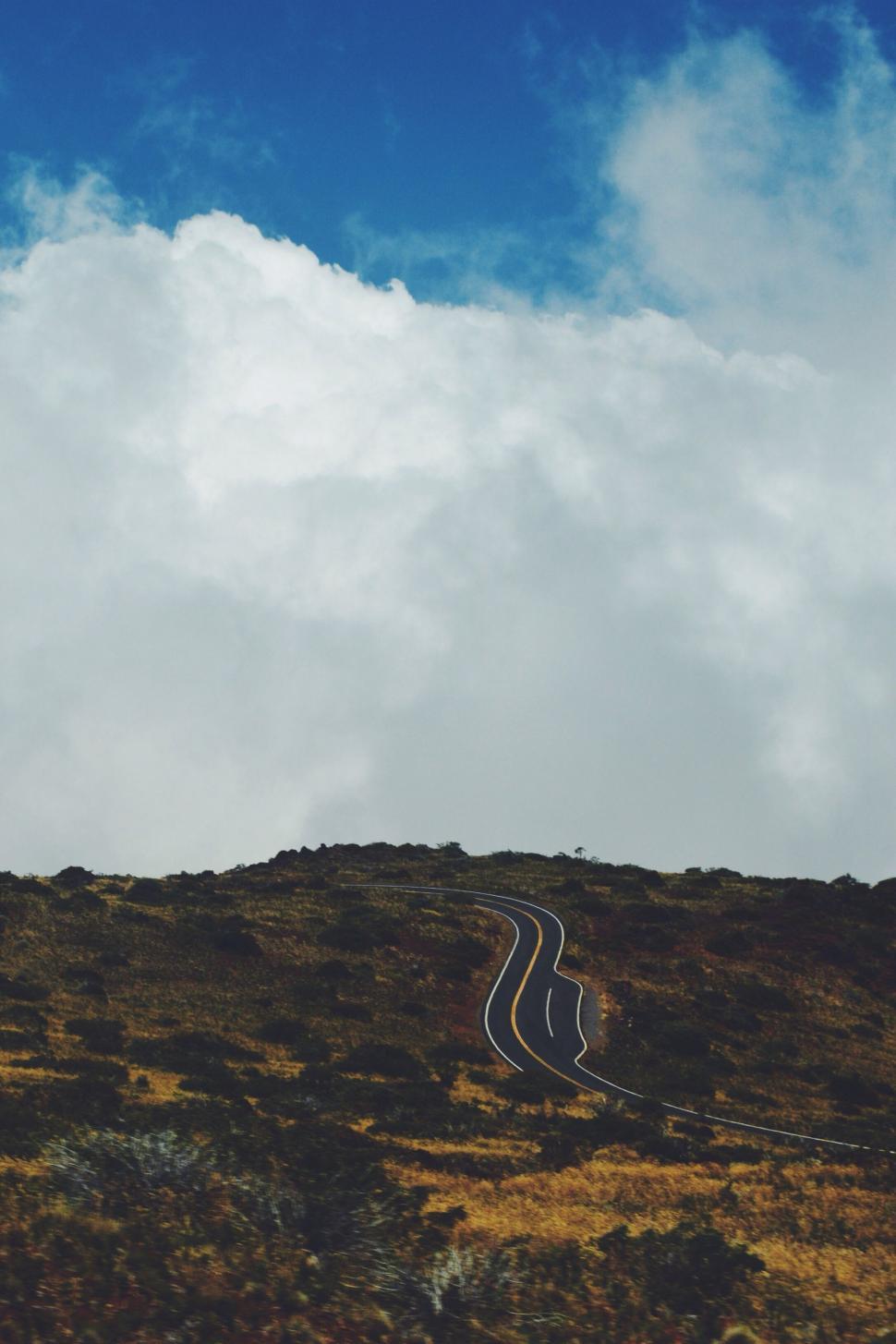 Free Image of Winding Road Ascending Hill Under Cloudy Blue Sky 