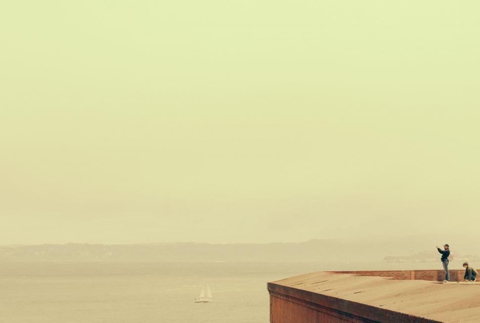 Free Image of Two People Standing on a Ledge Overlooking a Body of Water 