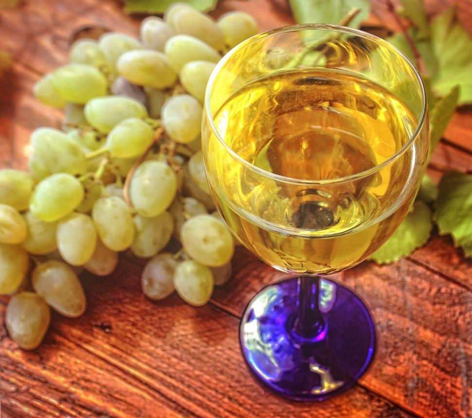 Free Image of Glass of white wine and a bunch of grapes in the background 
