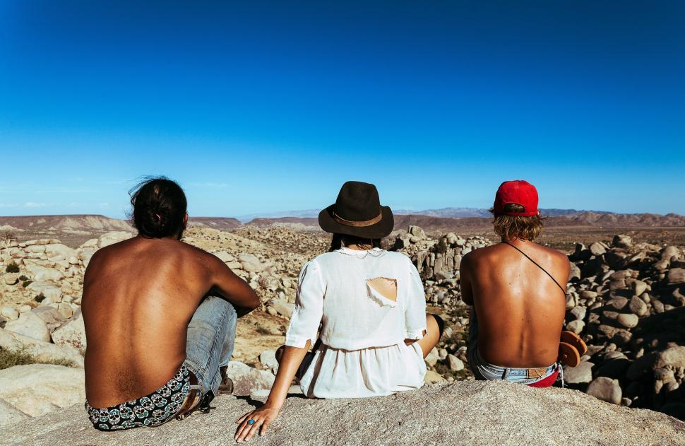 Free Image of Three People Sitting on a Rock in the Desert 