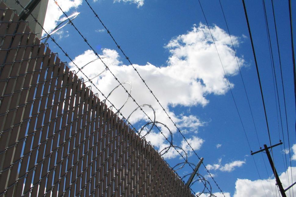 Free Image of fence razor wire barb barbed telephone pole power line blue sky clouds security secure deterrent spiral 
