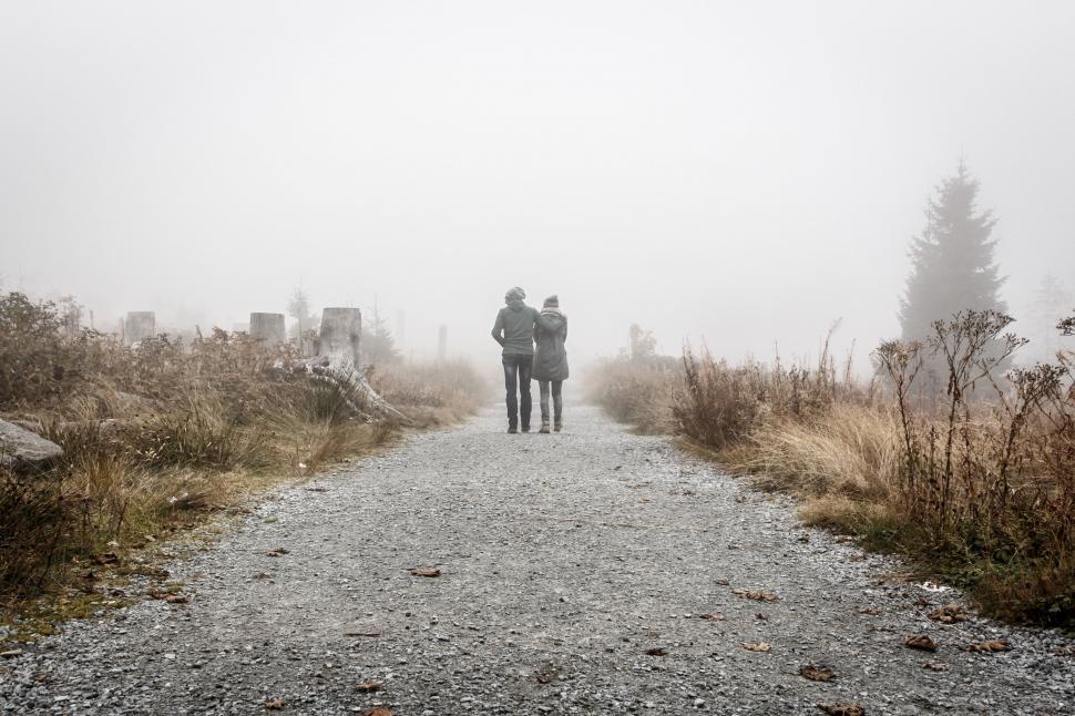 Free Image of Two People Walking Down a Dirt Road in the Fog 