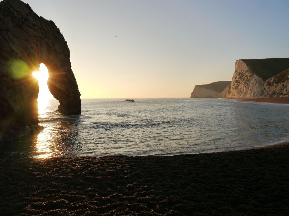Free Image of Sun Setting Behind Rock Formation on Beach 
