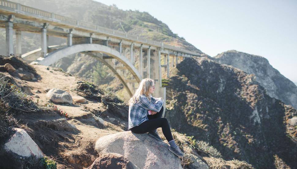 Free Image of Woman Sitting on Rock Near Bridge 