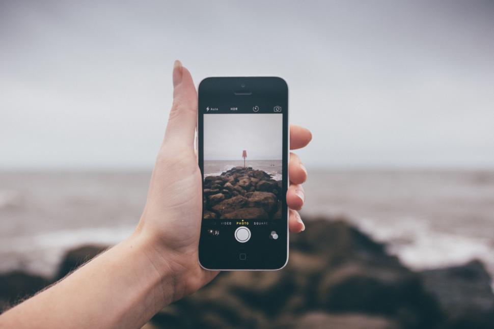 Free Image of Hand Holding Cell Phone Capturing Ocean View 