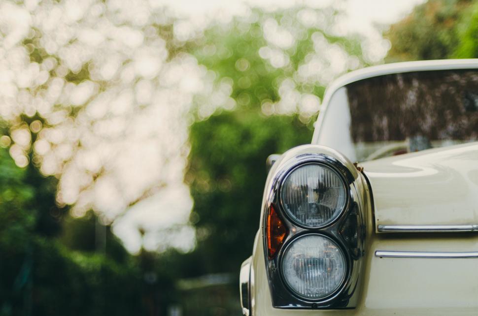 Free Image of Close Up of Car Headlight With Trees in Background 