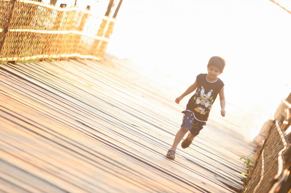 Free Image of Little Boy Running Across Wooden Bridge 