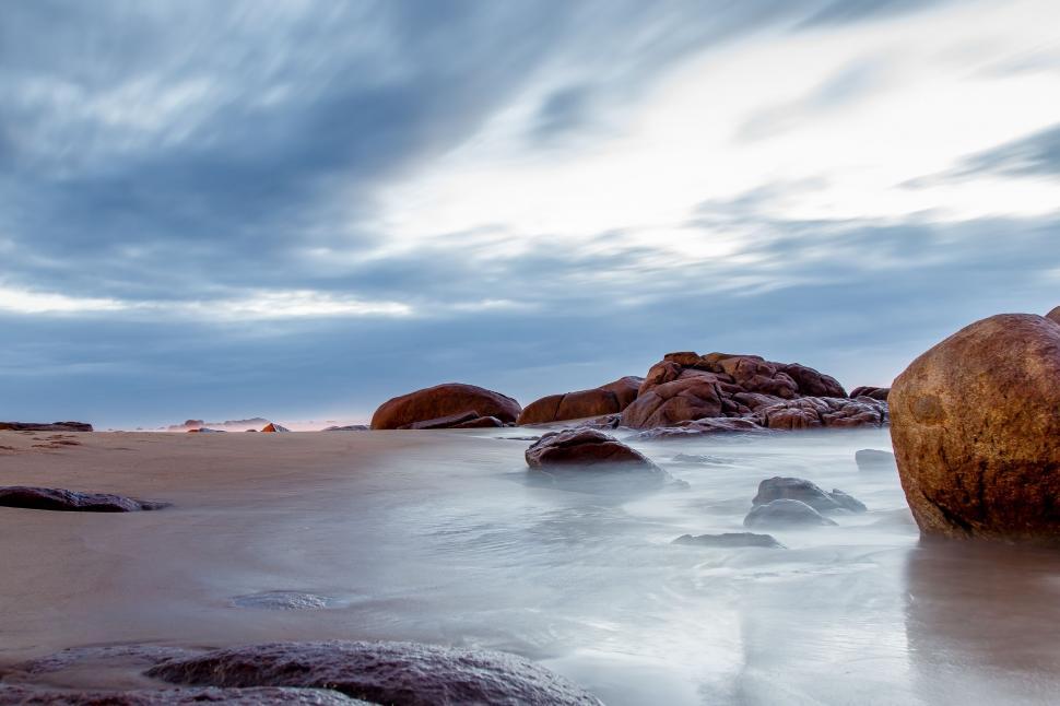 Free Image of Rocks and Water on Beach Under Cloudy Sky 