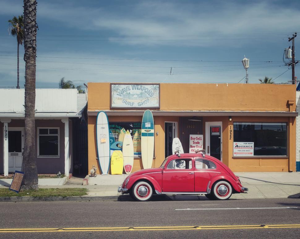 Free Image of Red Car Parked in Front of Surf Shop 
