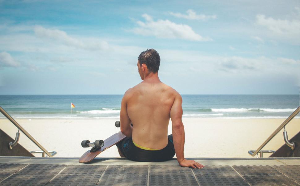 Free Image of Man Sitting on Beach With Skateboard 