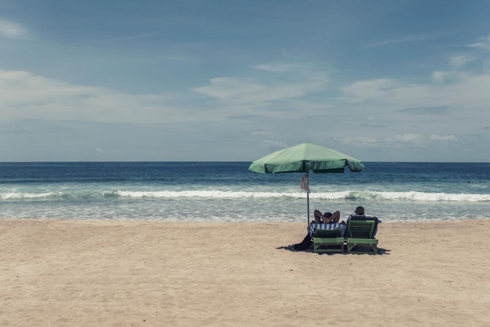 Free Image of Two People Sitting Under an Umbrella on a Beach 