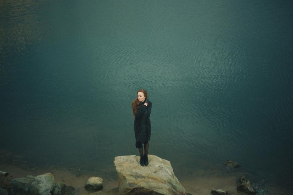 Free Image of Woman Standing on Top of Rock Next to Water 