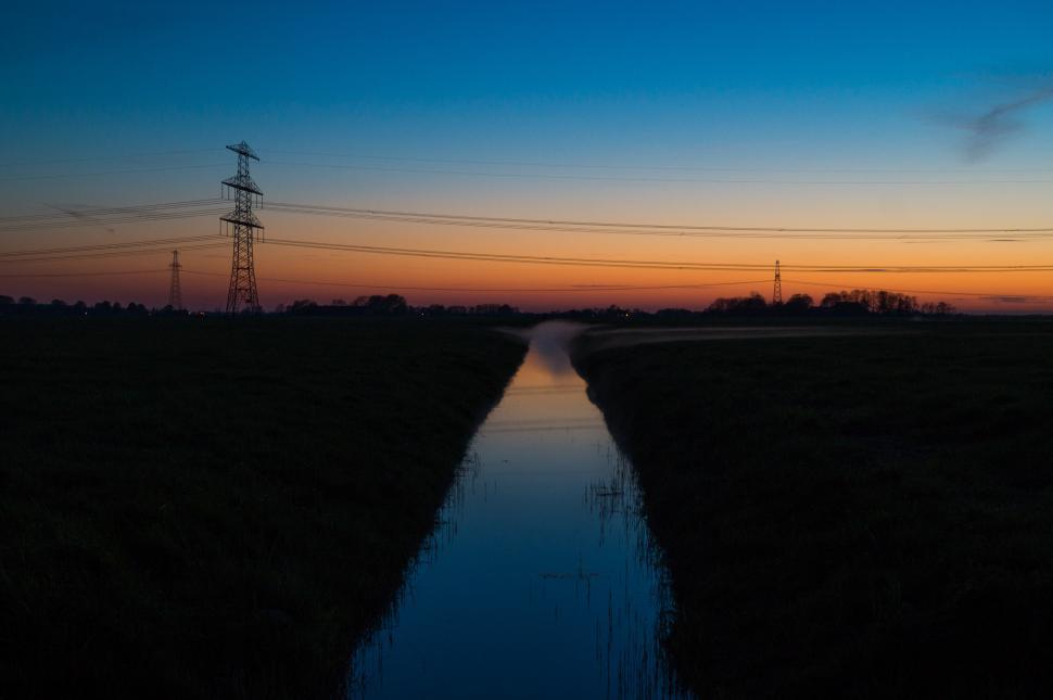 Free Image of River Flowing Through Field Next to Power Lines 