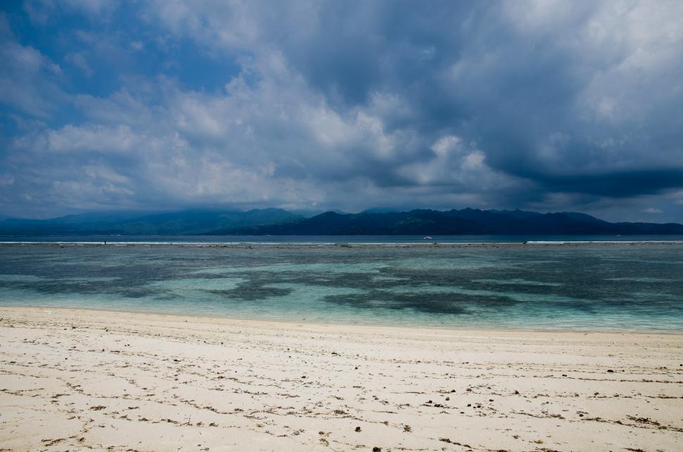 Free Image of Sandy Beach With Blue Water Under a Cloudy Sky 