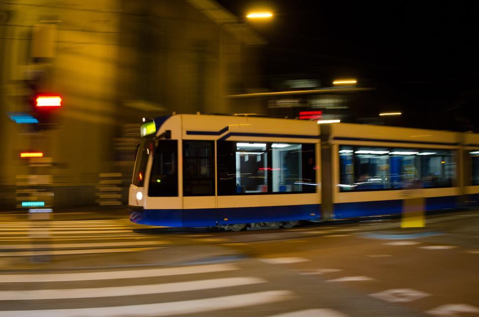Free Image of Blue and White Train Traveling Down a Street at Night 