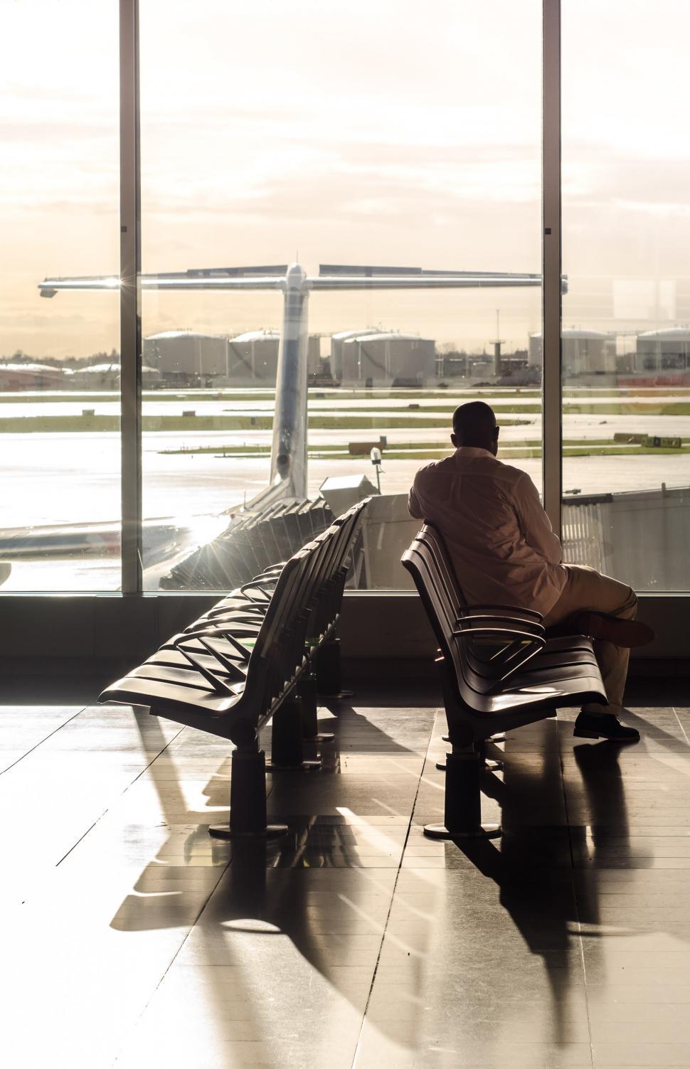 Free Image of Man Sitting on Bench Looking Out Airport Window 
