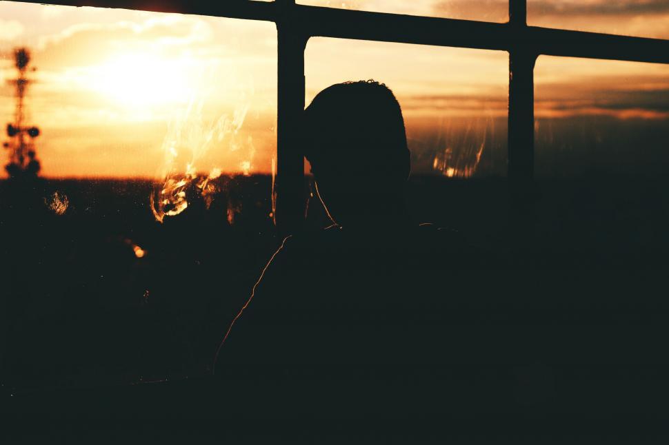 Free Image of Person Looking Out a Window at Sunset 