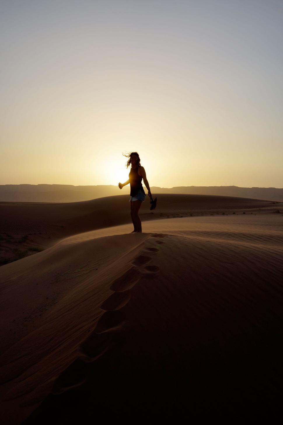 Free Image of Woman Walking Across Desert at Sunset 