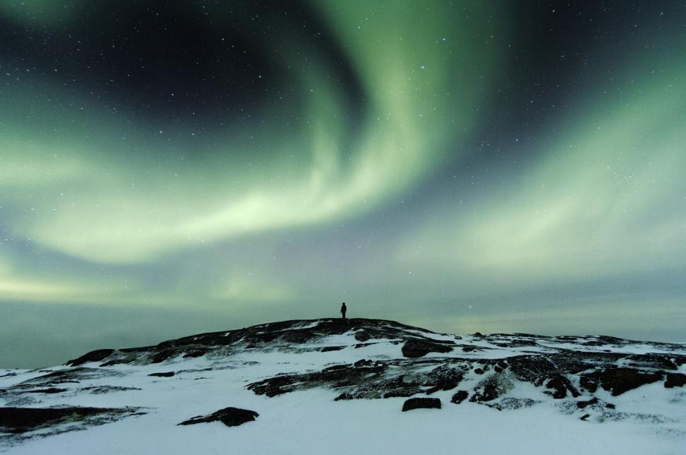 Free Image of Man Standing on Snow Covered Hill Under Green and White Aurora 