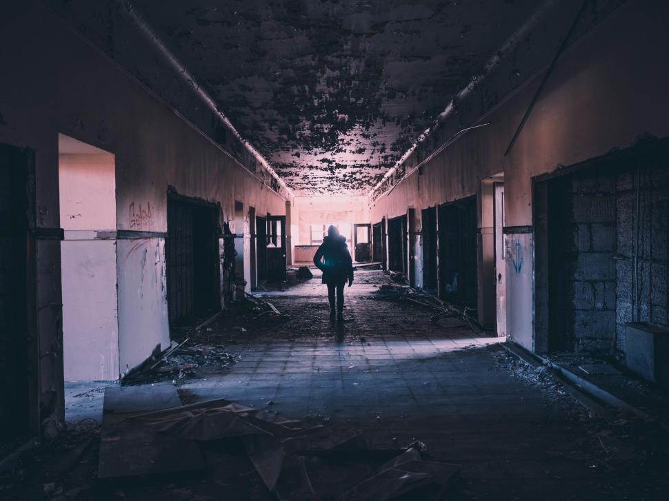 Free Image of Person Walking Down Dark Hallway in Abandoned Building 
