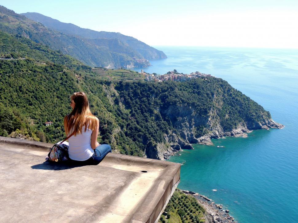 Free Image of Woman Sitting on Ledge Overlooking Body of Water 