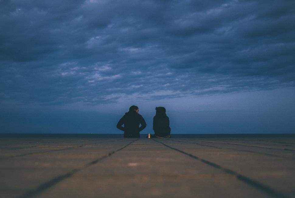 Free Image of Two People Sitting Under a Cloudy Sky 