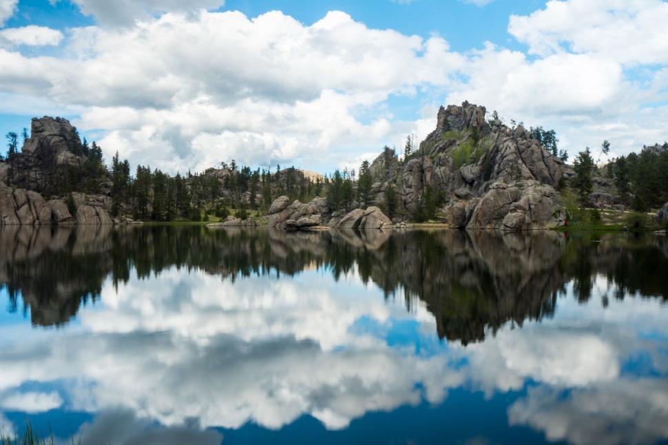 Free Image of A Lake Surrounded by Rocks and Trees Under a Cloudy Blue Sky 