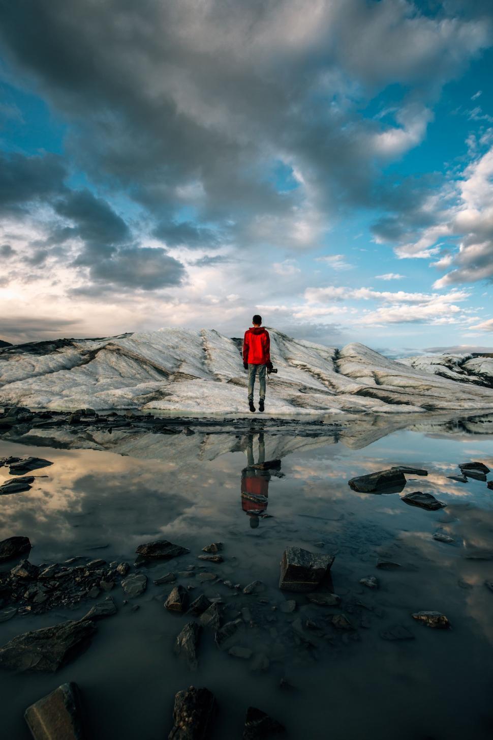 Free Image of Man in Red Jacket Standing on Rock Covered Beach 