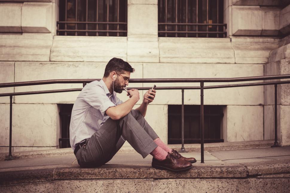 Free Image of Man Sitting on Steps Looking at Cell Phone 
