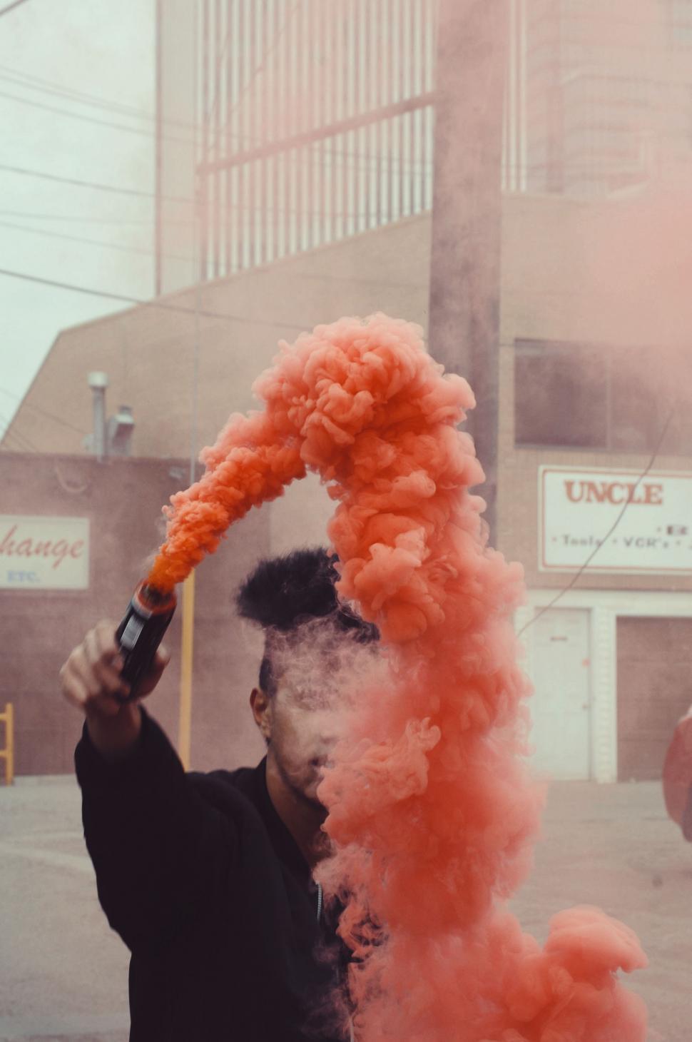 Free Image of Man Holding Pipe Emitting Orange Smoke 