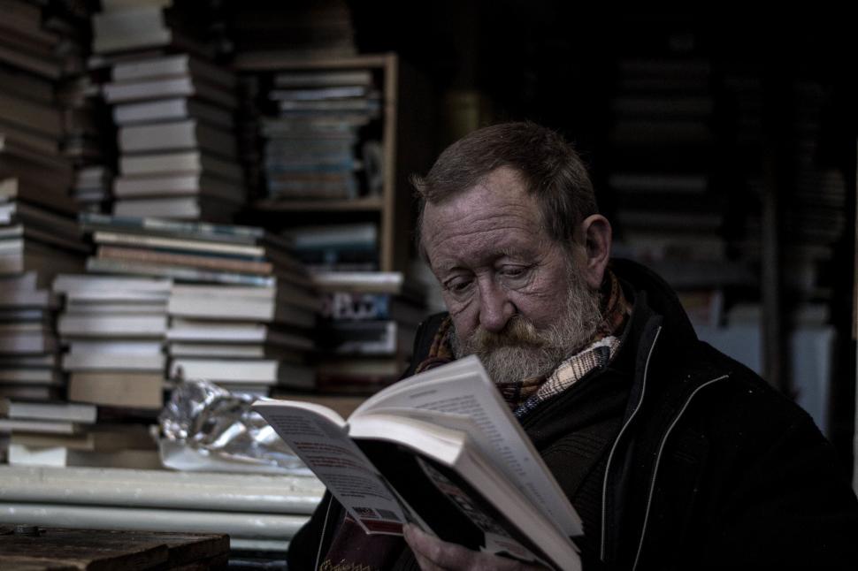 Free Image of Man Reading Book in Front of Stack of Books 
