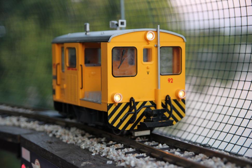 Free Image of Yellow Train Traveling Down Train Tracks Next to Fence 