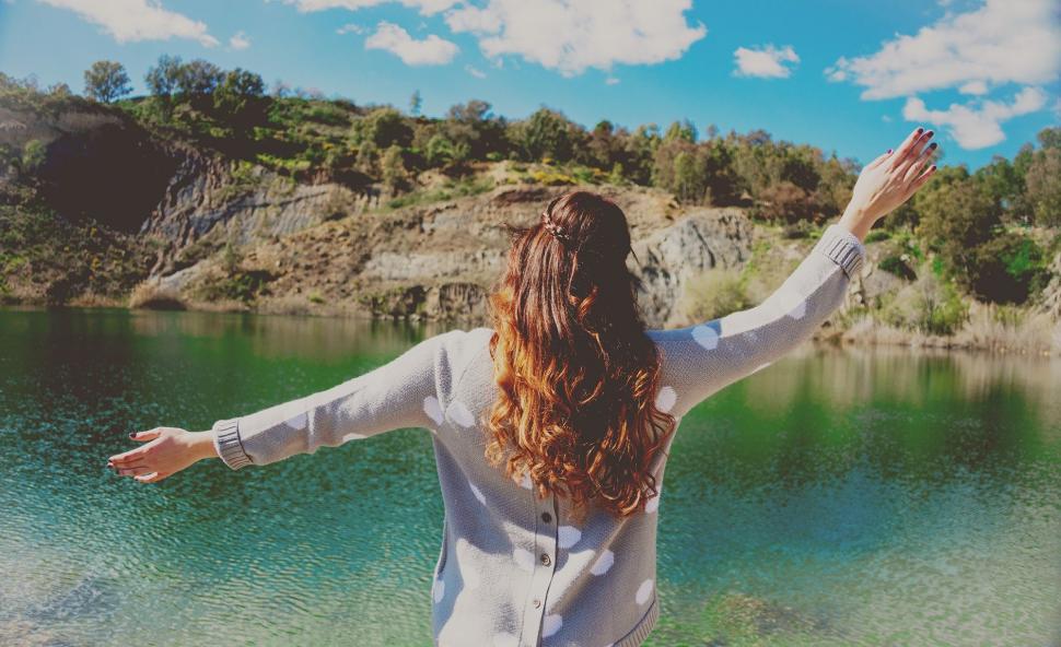 Free Image of Woman Standing With Arms Outstretched by Lake 