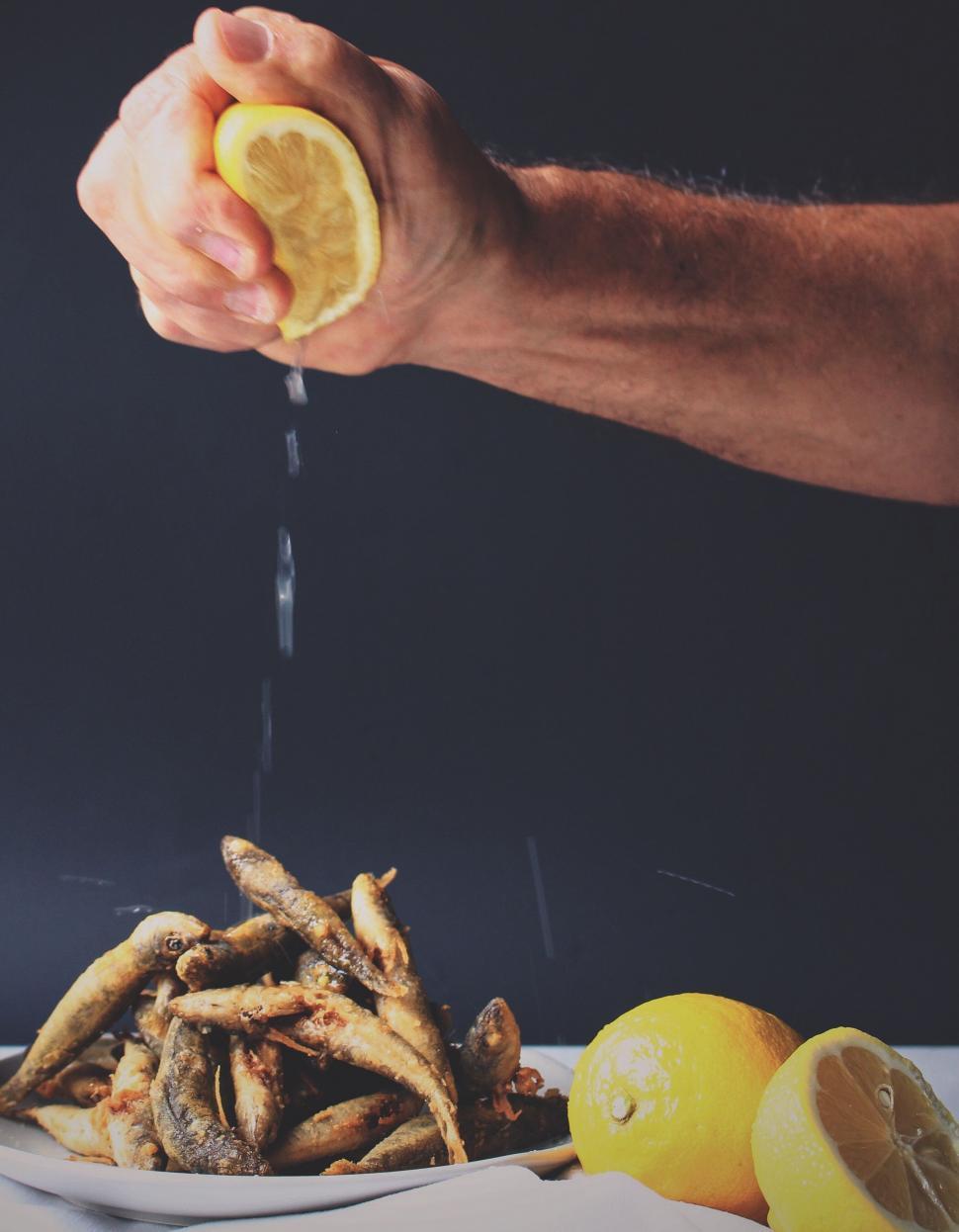 Free Image of Man Sprinkling Lemon on Plate of Fried Fish 