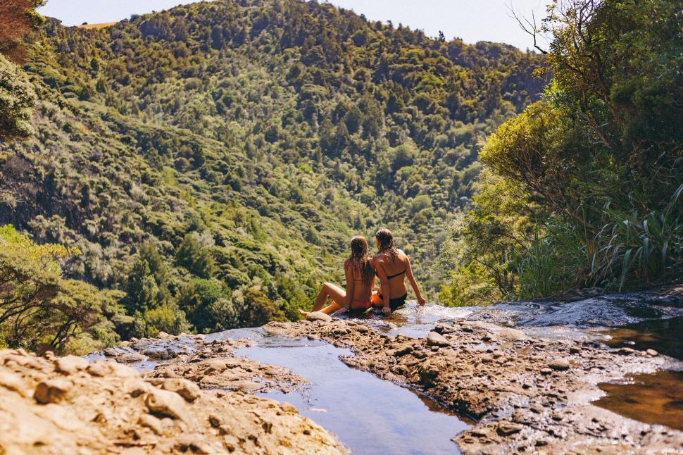 Free Image of Two People Sitting on a Rock in the Middle of a River 