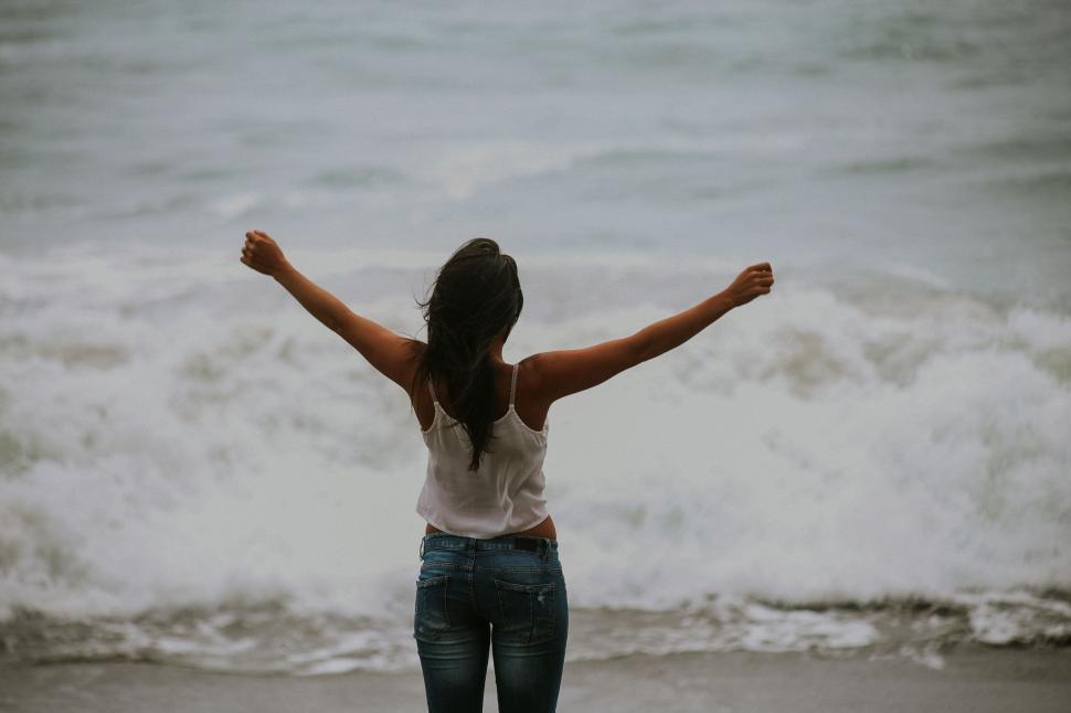 Free Image of Woman Standing on Beach With Arms Outstretched 