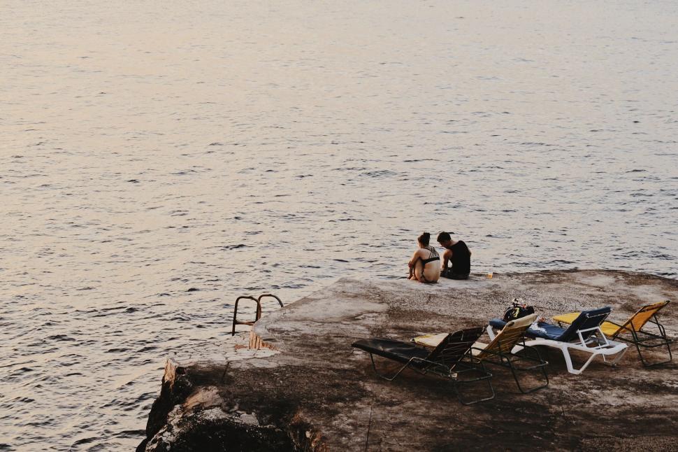 Free Image of Couple Sitting on Rock by Water 