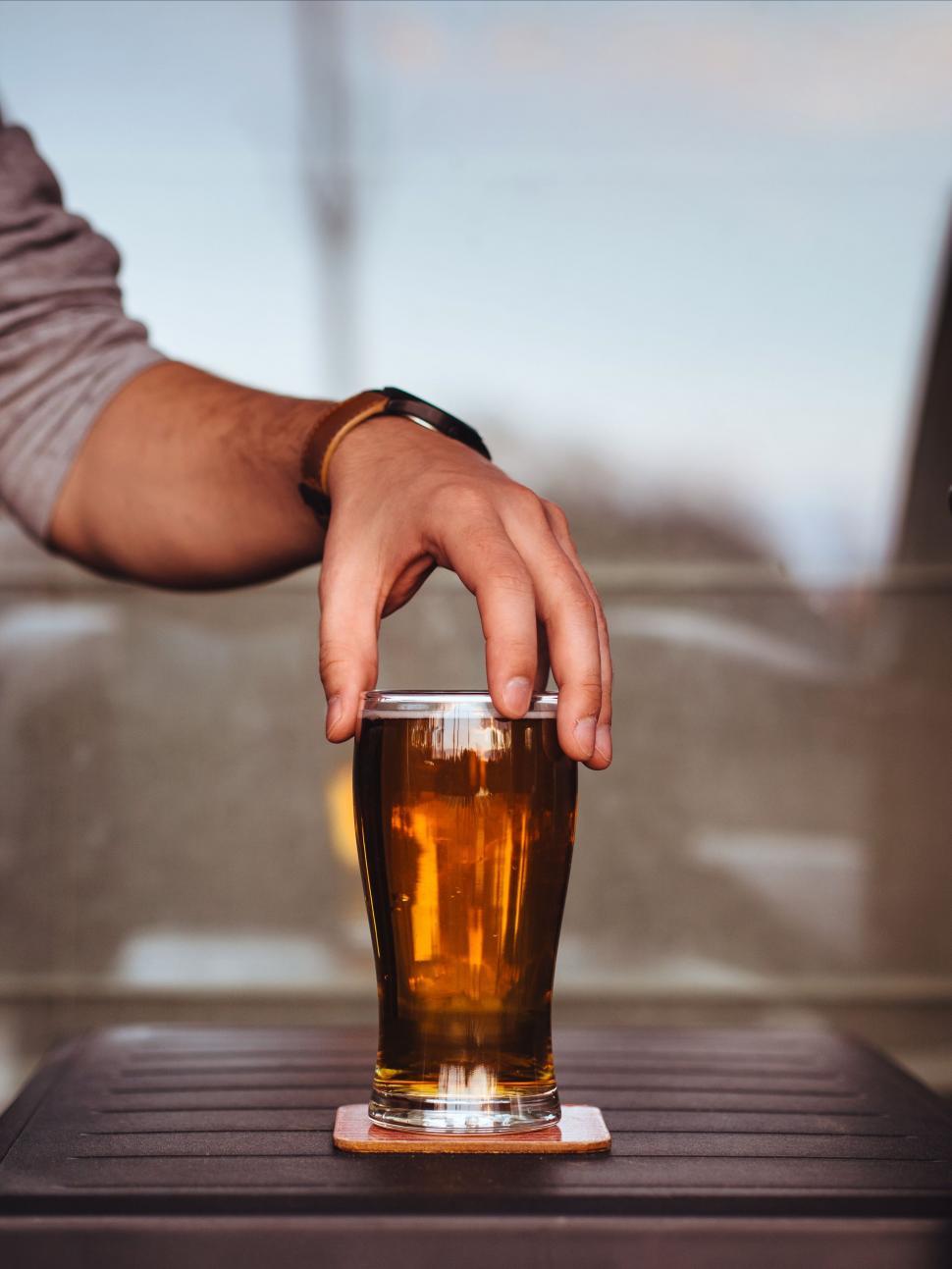 Free Image of Man Holding Glass of Beer on Table 