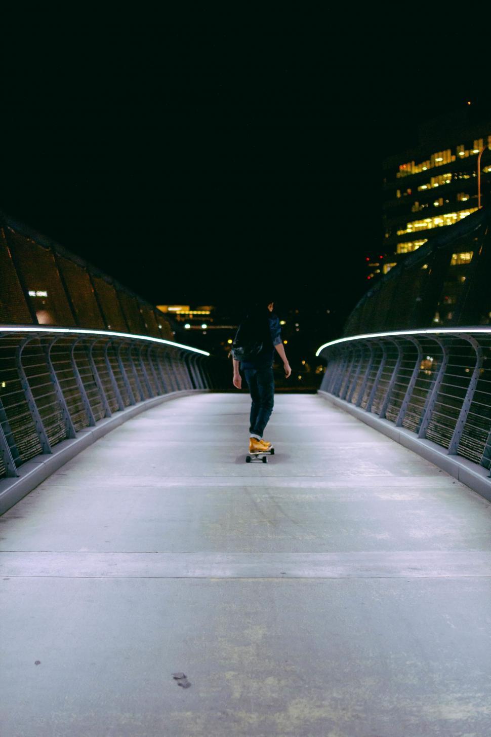 Free Image of Man Riding Skateboard Across Bridge at Night 